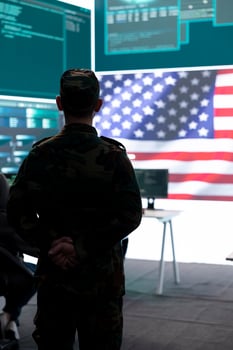 American military personnel supervising cyber warfare activity in high tech office, examine top secret intelligence on big screen. Governmental experts manage hybrid war, digital conflict prevention. photo