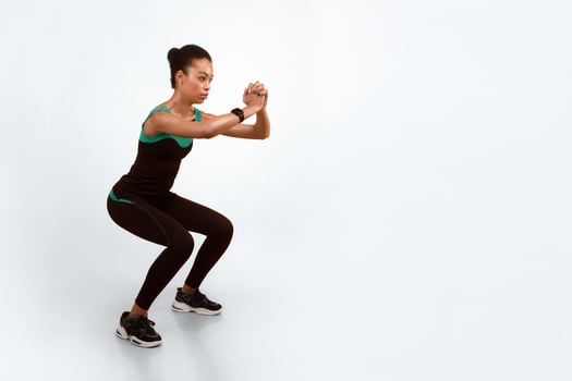 Workout Conept. African American Fitness Woman Doing Deep Squat Exercise Over Yellow Studio Background. photo