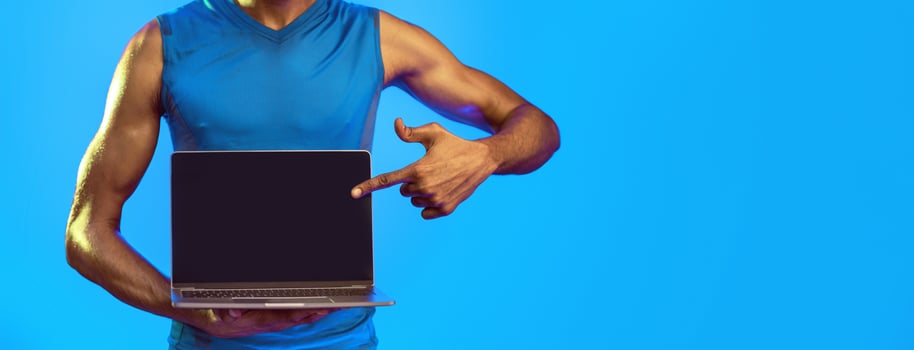 Online Workout. Fitness Guy Showing Laptop Empty Screen Standing On Blue Studio Background. Cropped, Mockup photo