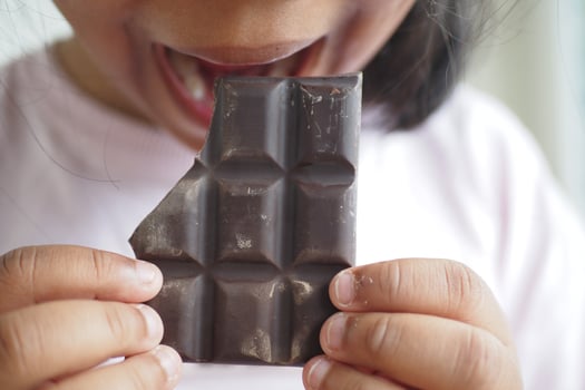 A young child is happily enjoying a delicious piece of chocolate bar outdoors in a playful manner photo