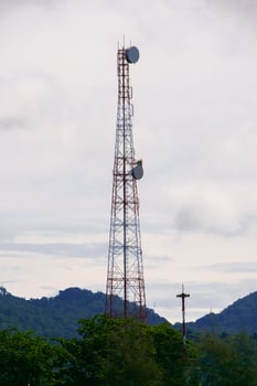 Tall Communication Tower Against a Cloudy Sky with Lush Greenery and Distant Hills in the Background photo