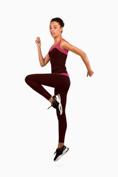 Fitness And Workout. Afro Girl Jumping Exercising During Sport Training Looking At Camera On White Studio Background. Vertical, Full Length photo