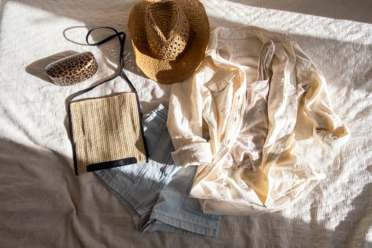 Casual summer outfit arrangement on bed, featuring light clothing and stylish hat. photo