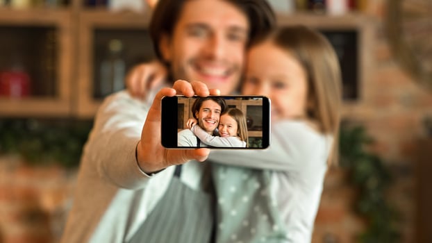 Happy dad and daughter taking selfie on smartphone while cooking at kitchen, little girl and her father hugging and smiling at camera, selective focus photo