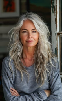 Stylish woman with long gray hair relaxing indoors A confident woman with long gray hair stands indoors, wearing a comfortable sweater, exuding a relaxed and stylish vibe. photo
