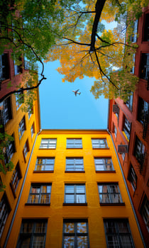 Vibrant courtyard with trees and planes A vibrant courtyard framed by autumn leaves and colorful buildings under a clear blue sky, showcasing an airplane flying overhead. photo