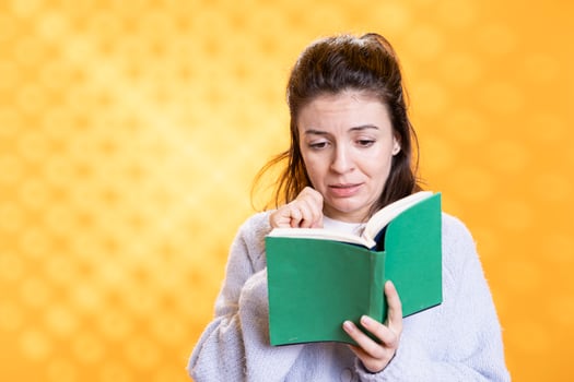 Woman sobbing while reading sad book, enjoying hobby during leisure time. Bookaholic person with novel in hands weeping, enthralled by emotional story, isolated over studio background photo