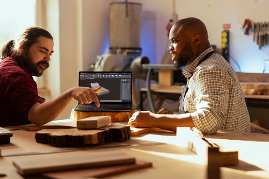 Cabinetmaker and colleague using CAD software on laptop to design wooden objects. Master carpenter and apprentice using program on notebook to plan furniture assembling in joinery photo