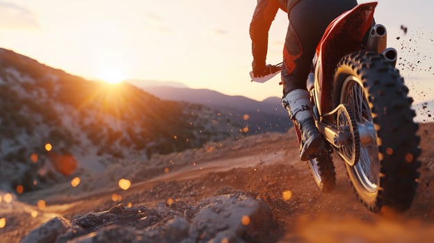 Motocross rider speeding through a rocky terrain at sunset in a mountainous landscape photo