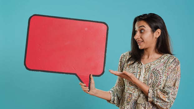 Smiling indian woman holding red speech bubble sign of empty copy space for message. Joyous person presenting thought bubble cardboard used as promotion concept, studio background, camera A photo