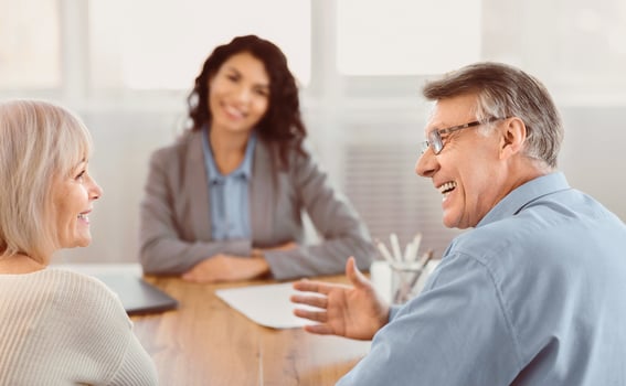 Good News. Happy senior couple looking at each other and listening to saleswoman sitting at the desk in the background photo