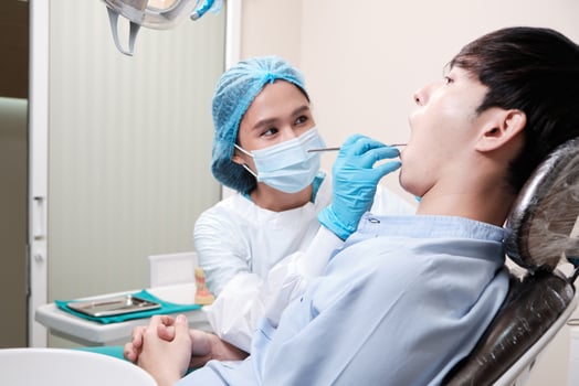 Asian female dentist examine young male patient teeth and toothache stomatology in dental clinic, well-being hygiene checks, and professional orthodontic healthcare work in doctor's office hospital. photo