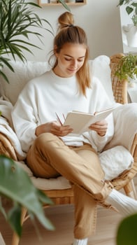 Young woman sitting in a cozy chair in a plant-filled room, enjoying her time writing in a notebook during the afternoon photo