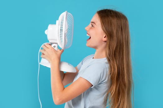 Child girl enjoying cool air. Child and fan on blue background. Room temperature regulation photo