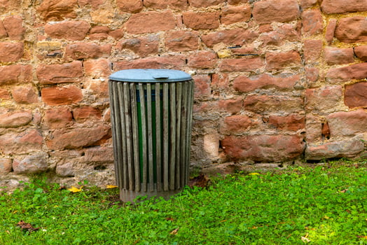 A wooden trash can sits against a brick wall, surrounded by green grass photo