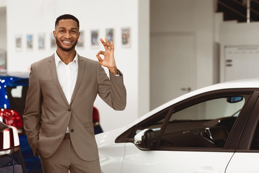 Car Sales. Smiling Black Salesman Gesturing Okay Standing In Luxury Auto Store. Free Space For Text photo