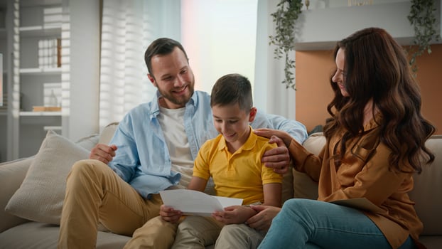 Excited Happy Caucasian family parents mother father child son receive paper notice letter at home on couch kid boy reading good news celebrating victory enjoying success great successful exam result photo