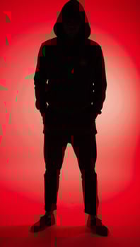 Man in hood with no visible face silhouetted against red background photo