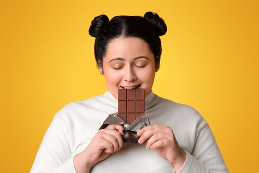 Chocoholic Concept. Young Plus Size Girl Enjoying Eating Chocolate Bar, Standing With Closed Eyes On Yellow Background, Copy Space photo