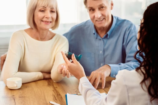 Asthma Attacks. Unrecognizable nurse giving blue inhaler to smiling mature couple, selective focus photo
