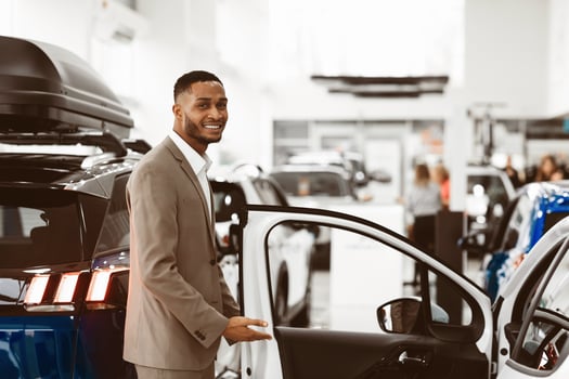 African Dealer Man Showing Car Opening Door And Inviting To Test New Auto Standing In Automobile Dealership Store. Selective Focus photo