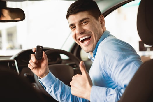 Happy Man Showing New Car Key To Camera Gesturing Thumbs Up Sitting In Auto In Dealership Store photo