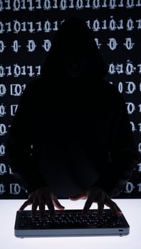 A hooded criminal silhouetted while hacking on binary code background cybercrime concept photo