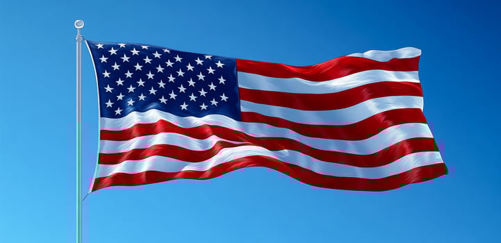 American flag waving proudly against a clear sky. The American flag flutters in the wind, showcasing its red, white, and blue colors against a bright blue sky. photo