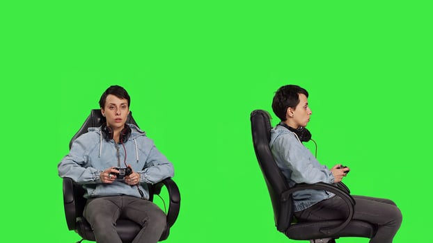 Happy gamer winning an online shooter competition in studio, playing e sport tournament against greenscreen backdrop. Young woman player celebrating her gaming victory on chair. Camera B. photo