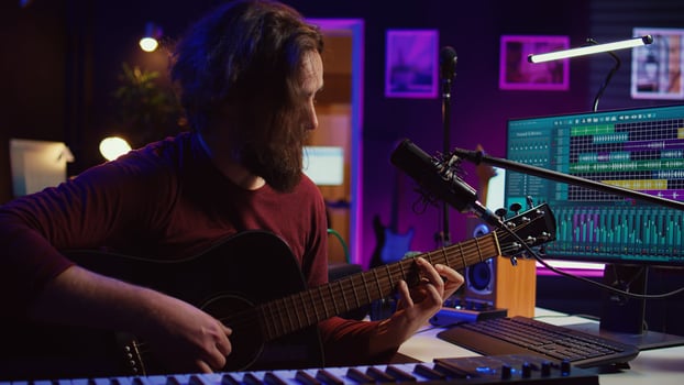 Artist composing a song with his acoustic guitar in home studio, recording notes and singing melody on microphone. Sound engineer mixing and mastering his tunes with stereo equipment. Camera B. photo