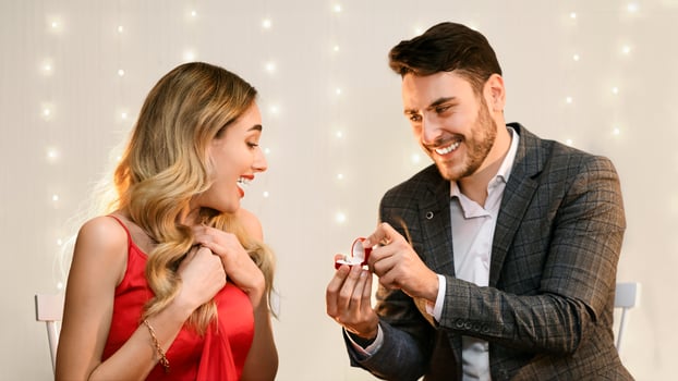 Loving man making proposal to his surprised girlfriend on romantic date in restaurant, presenting engagement ring photo