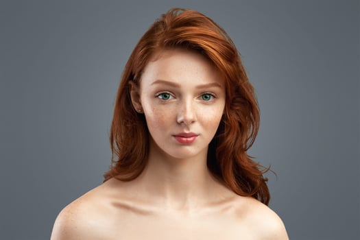 Youth Bodycare. Pretty Teenager Girl With Loose Red Hair Posing Wrapped In Towel Looking At Camera Standing Over White Studio Background. Headshot Of Young Adolescent Female photo
