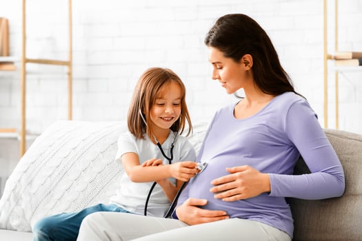 Little pretty girl listening belly of her pregnant mother through stethoscope, playing doctor at home, free space. Family and new life concept. photo