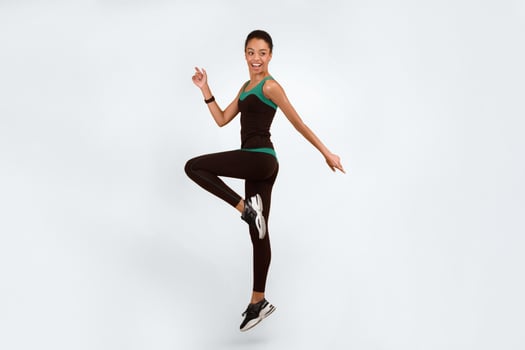 Fitness And Sport. Happy African American Girl Exercising Jumping Over Yellow Studio Background. Vertical, Full Length photo