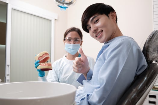 Asian female dentist explaining orthodontic care and whitening to young male patient with teeth model in dental clinic, well-being hygiene, and professional healthcare work in doctor office hospital. photo