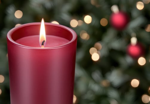 Glowing red candle in front of christmas tree photo