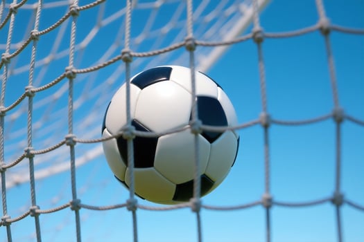 Soccer Ball Flying into Goal Net Against Blue Sky photo