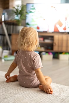 A small blonde baby girl sitting on the floor at home and wathing TV photo