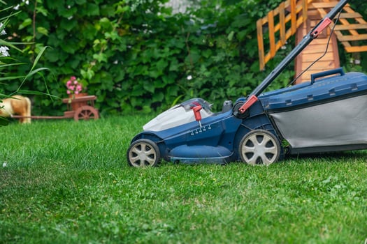 A lawn mower is cutting green grass, the gardener with a lawn mower is working in the backyard, a side view. photo
