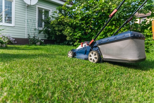 A lawn mower is cutting green grass, the gardener with a lawn mower is working in the backyard, a side view. photo