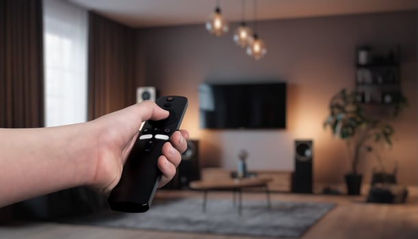 Hand holding a remote control, adjusting smart home devices in a modern living room. Concept of home automation, controlling lights, curtains, and smart speakers for a comfortable photo