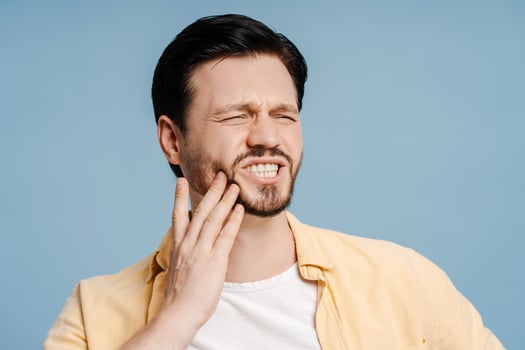 Young bearded man suffering from strong toothache, looking away isolated on blue background photo