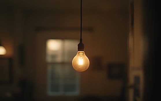 A vintage-style Edison light bulb hangs illuminated in a dark room, casting a warm glow against shadowy walls, creating a cozy atmosphere photo