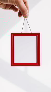 hand holding a red frame with a white space photo