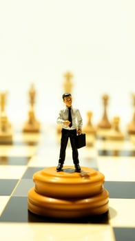 miniature businessman stands atop stacked chess pieces photo
