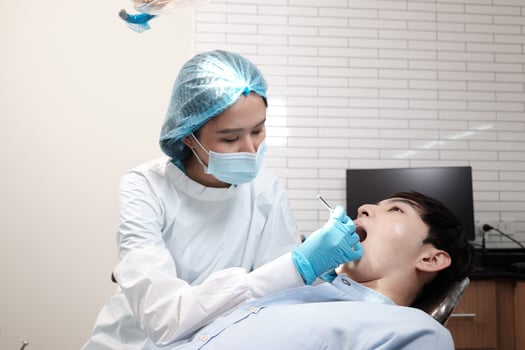 Asian female dentist examine young male patient teeth and toothache stomatology in dental clinic, well-being hygiene checks, and professional orthodontic healthcare work in doctor's office hospital. photo