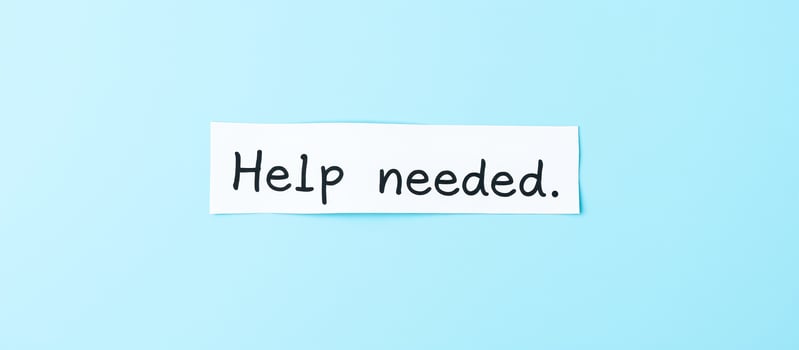 white paper note with the words help needed on a blue background photo