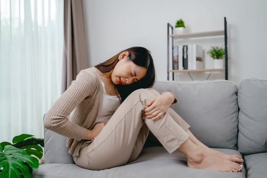 The woman with a stomachache is holding her stomach in pain, sitting on the sofa in the living room. photo