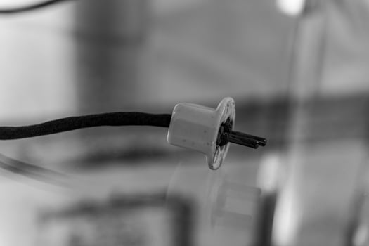 A close-up of a single, white, three-pronged electrical plug with a black cord photo