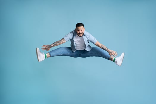 Happy man jumping with legs spread on blue background photo